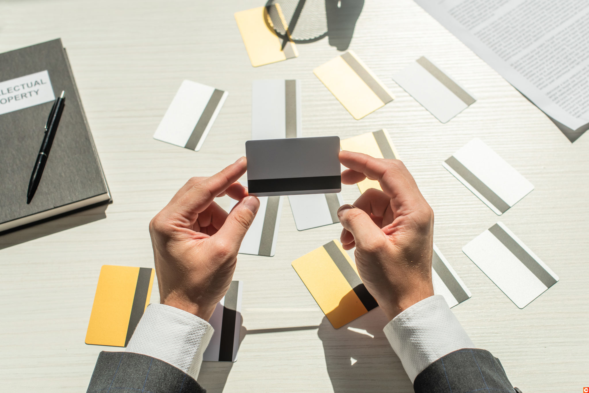 Cropped view of businessman holding credit card near notebook and business document on white textured background